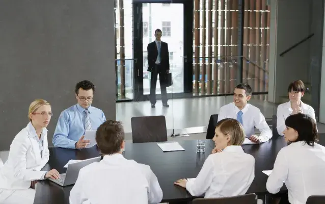 Des collègues en réunion d'affaires dans un bureau tandis qu'un homme attend derrière les portes en verre transparentes