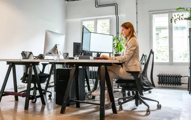 Une femme seul assise à un bureau face à deux écrans d'ordinateur.
