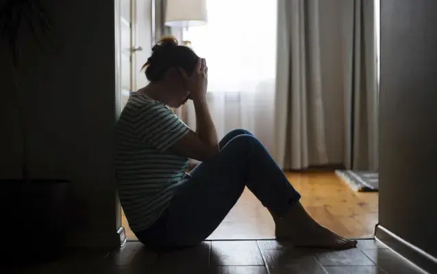 Silhouette d’une femme triste assise par terre, couvrant le visage avec les mains