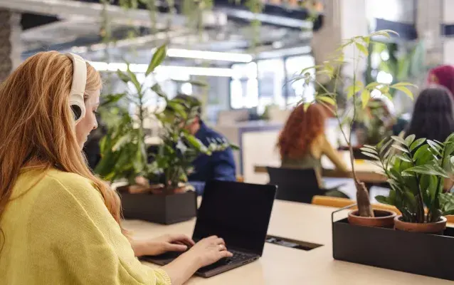 Jeune employé de bureau portant des écouteurs tapant sur un ordinateur portable dans un espace de travail vert