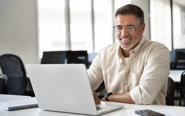 homme avec chemise beige et lunettes qui travaille avec un ordinateur portable