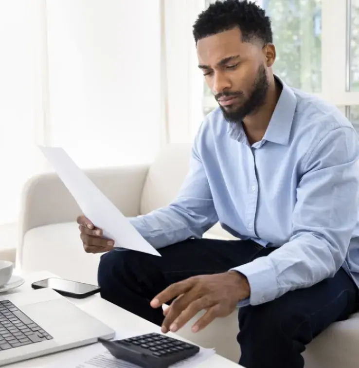 Homme qui fait des calcules avec sa calculatrice et des papiers en main devant son ordinateur.