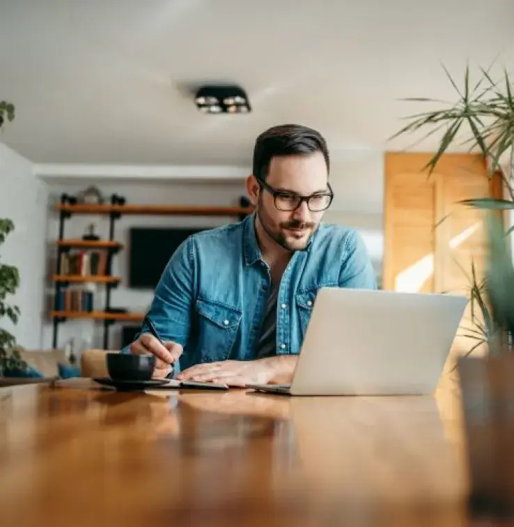 homme avec lunette prenant des notes devant son ordinateur à la maison