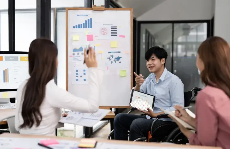 Une équipe diversifiée de jeunes professionnels, dont un homme en fauteuil roulant, collabore et discute de stratégies commerciales, d’analyses de marché et de planification de projets dans un cadre de bureau moderne.
