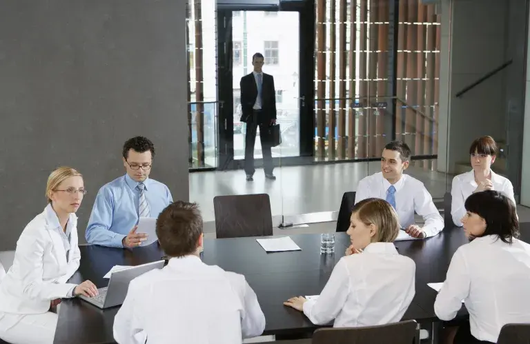 Des collègues en réunion d'affaires dans un bureau tandis qu'un homme attend derrière les portes en verre transparentes