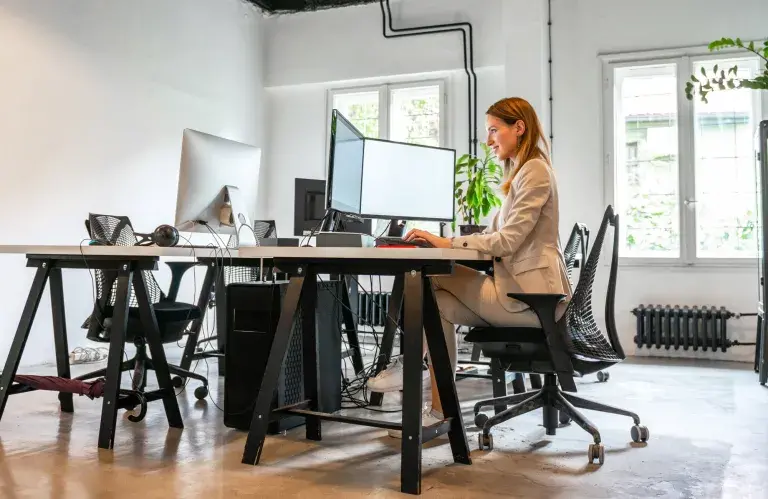Une femme seul assise à un bureau face à deux écrans d'ordinateur.
