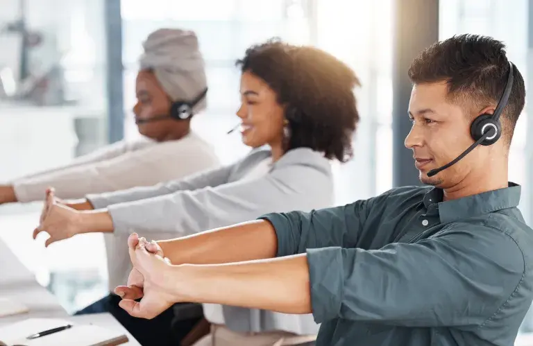 Groupe d’agents de télémarketing de centre d’appels tendant les bras tout en travaillant ensemble dans un bureau. Un consultant hispanique prend une pause pour se préparer à faire fonctionner le service d’assistance pour le service à la clientèle