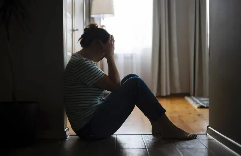 Silhouette d’une femme triste assise par terre, couvrant le visage avec les mains