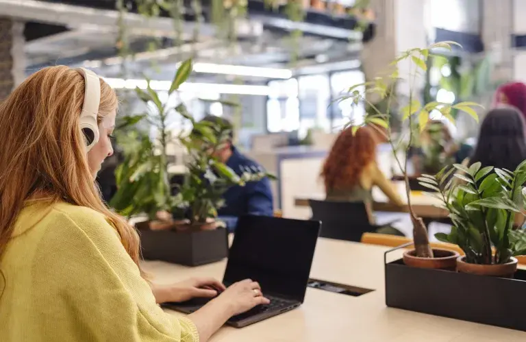 Jeune employé de bureau portant des écouteurs tapant sur un ordinateur portable dans un espace de travail vert