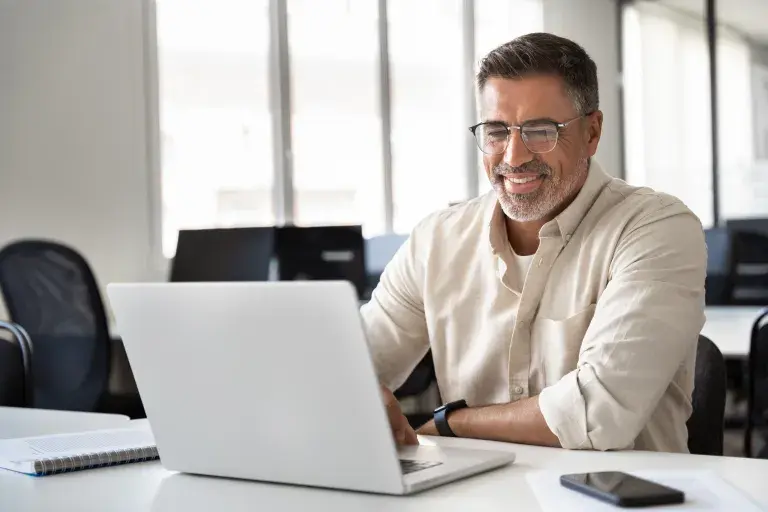 homme avec chemise beige et lunettes qui travaille avec un ordinateur portable