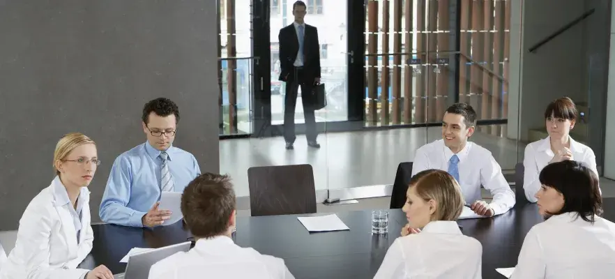 Des collègues en réunion d'affaires dans un bureau tandis qu'un homme attend derrière les portes en verre transparentes