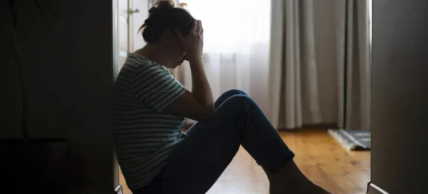 Silhouette d’une femme triste assise par terre, couvrant le visage avec les mains